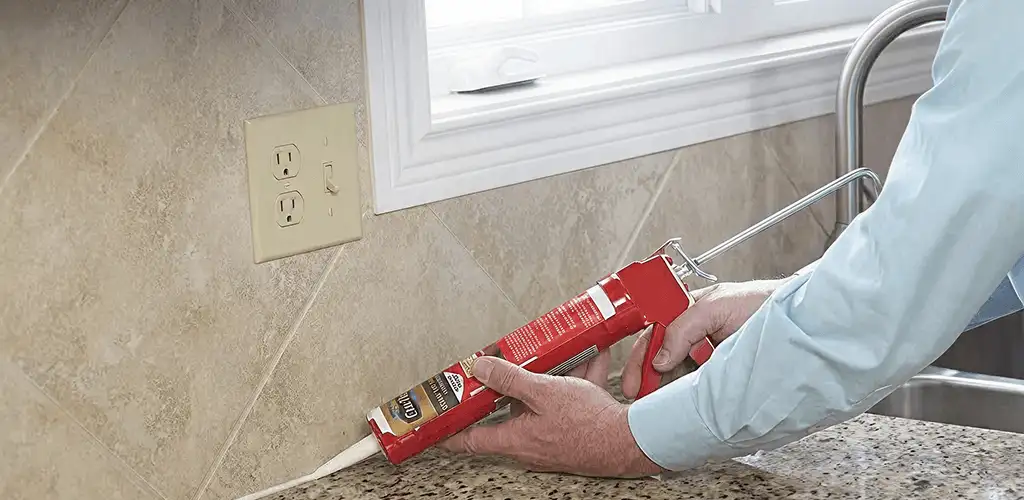 Handyman applying caulk along a kitchen backsplash and countertop seam in Rochester, NY